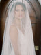 Very close portrait of the bride, the Grace English silk veil covering her face, showing a pearl earring and the slight texture of the silk tulle.