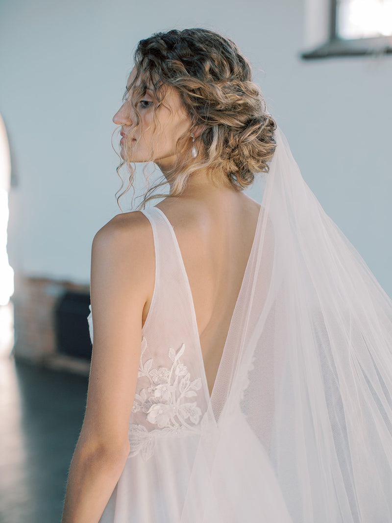 Close profile shot of the bride's head and back, showing her elegant low updo and the Grace silk wedding veil flowing down; blusher opened and worn at the back.