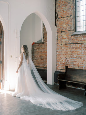 KAJA draped bridal cape veil styled with lace gown, photographed in an old church.