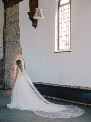 KAJA draped bridal cape veil styled with a lace gown and half up hairstyle.
