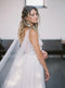 KAJA draped bridal cape veil styled with a lace gown, statement earrings, and half up hairstyle.