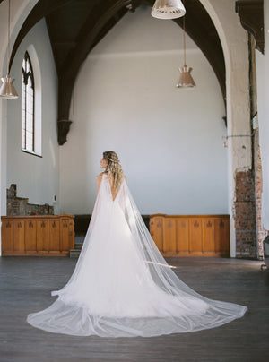 KAJA draped bridal cape veil styled with a lace gown and half up hairstyle.