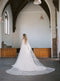 KAJA draped bridal cape veil styled with a lace gown and half up hairstyle.