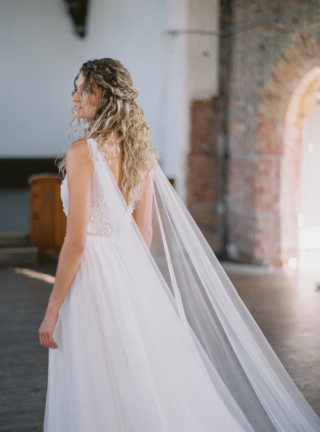 KAJA draped bridal cape veil styled with a lace gown and half up hairstyle.