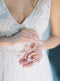 Bride's hands holding the pair of KYOTO Floral Bridal Earrings, showing the pink flower and pearl detail against her lace wedding dress.