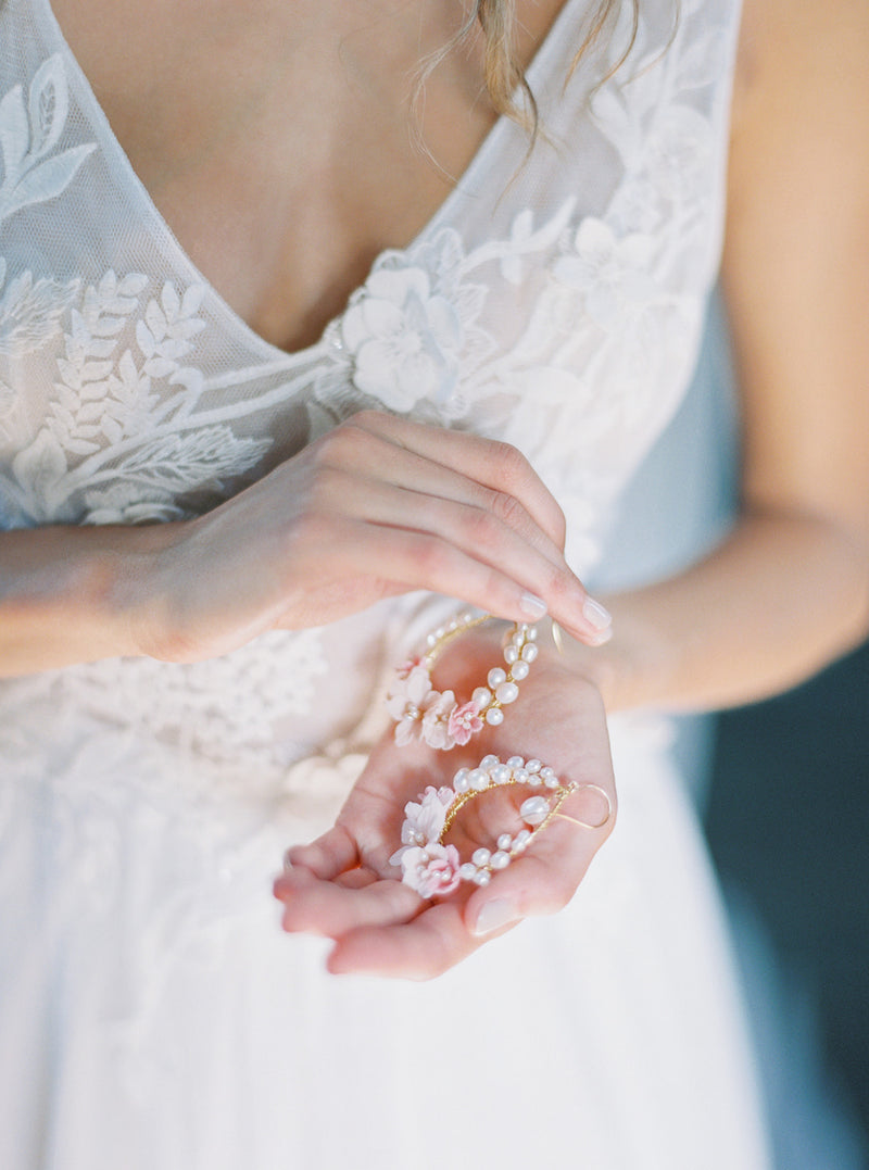 Bride's hands holding the pair of KYOTO Floral Bridal Earrings, showing the pink flower and pearl detail against her lace wedding dress.