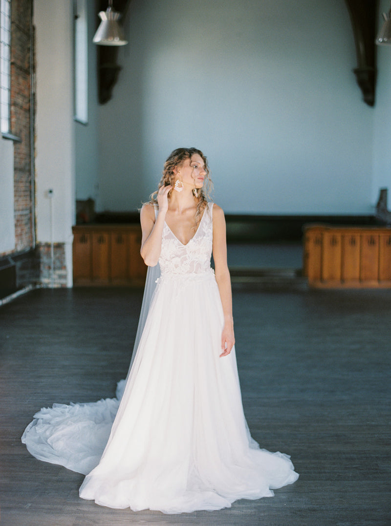 Full-length shot of a bride wearing the KYOTO Floral Bridal Earrings and a tulle bridal gown in a large, light-filled church.