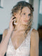 Portrait of a bride wearing the KYOTO Pearl and Floral Bridal Earrings, gently touching her curly hair.
