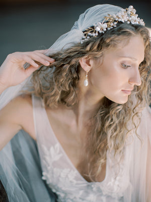 Profile view of a bride with curly hair wearing the elegant LYON drop earrings and a delicate pearl and gold floral bridal crown.