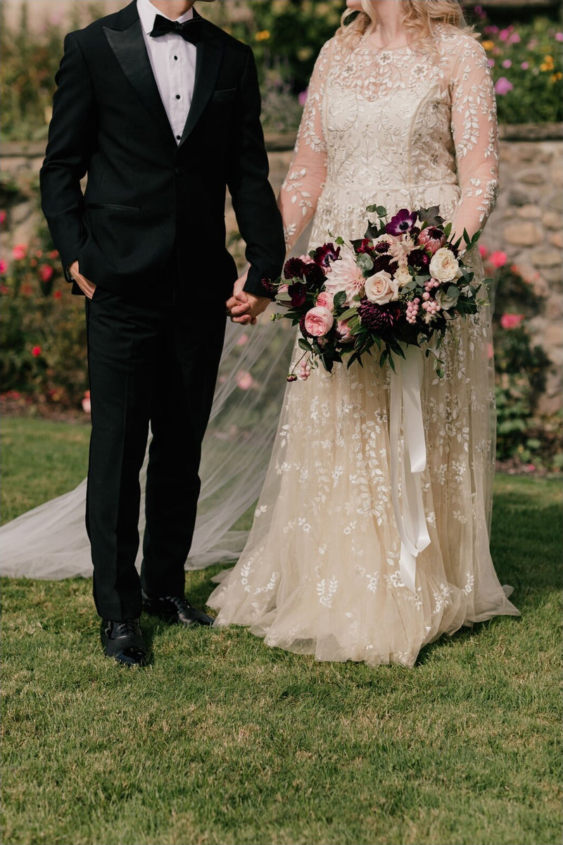 Close-up of the bride and groom holding hands on the grass, showing the sheer material of the Olivia veil pooling around the bride's lace gown.