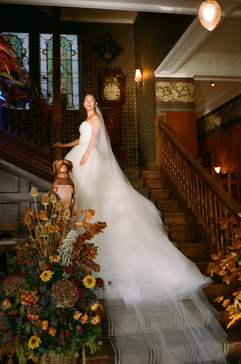 Bride ascending a wood staircase wearing a strapless gown and the Olivia long wedding veil, which dramatically trails down several stairs.