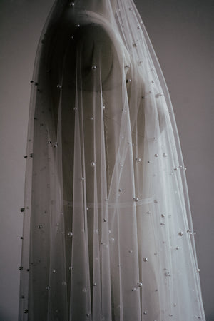 Side view of the sheer OPERA veil with scattered pearls flowing over a dress form.