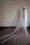 The OPERA Pearl Veil on a dress form, with train fanned out on a wooden floor, showcasing its cathedral length. 