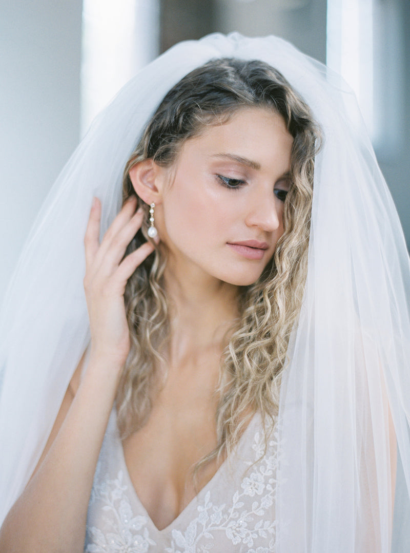 Portrait of a bride wearing the Rosanna full wedding veil with hair down, and the veil styled on the crown of her head.