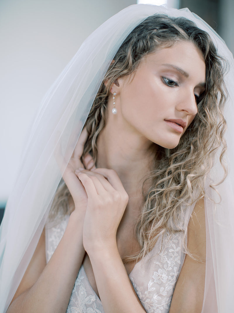 Portrait of a bride looking down while the the voluminous Rosanna wedding veil softly frames her face and curly hair.