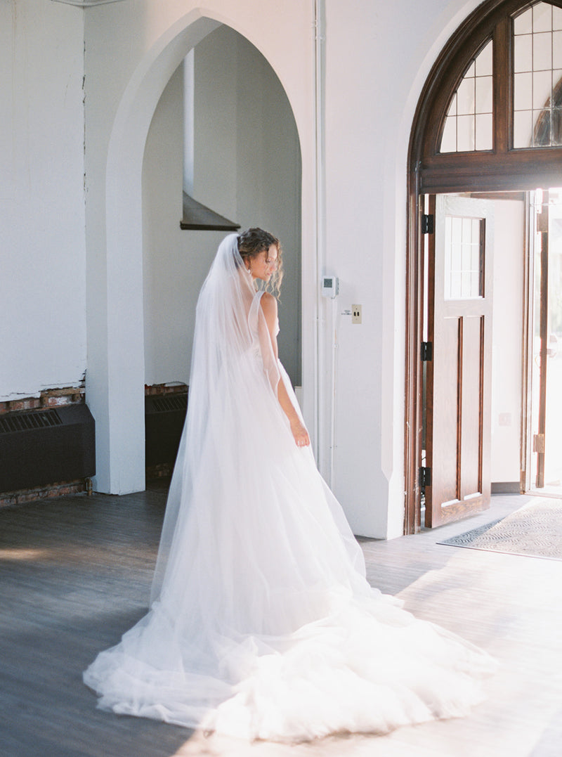 Bride standing in front of arched church doors, wearing the Rosanna full wedding veil and a lace wedding dress. 