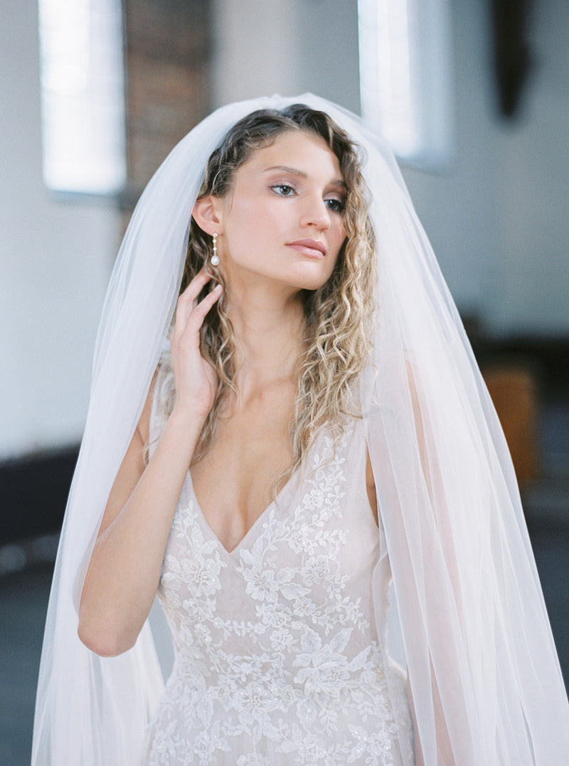 Close-up bridal portrait showing the Rosanna full veil draped over the bride's head and shoulders, highlighting the soft volume and sheer Whisper tulle.