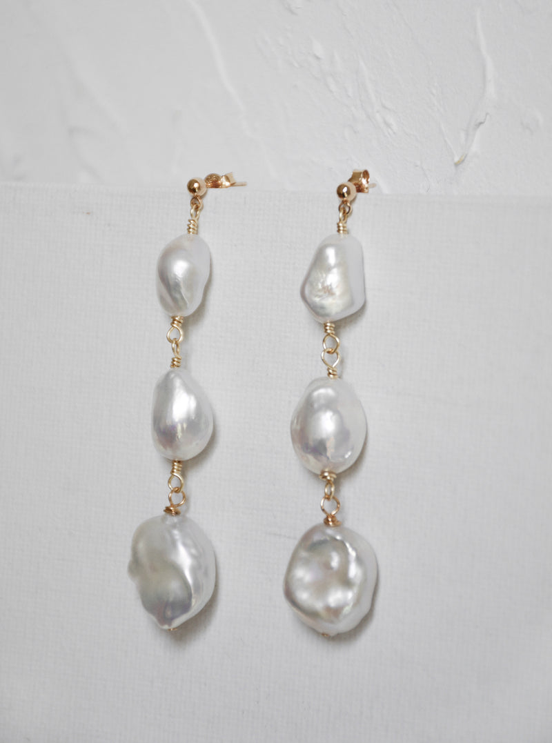 The Tia pearl drop earrings on a textured background. The pearls glow in the light.