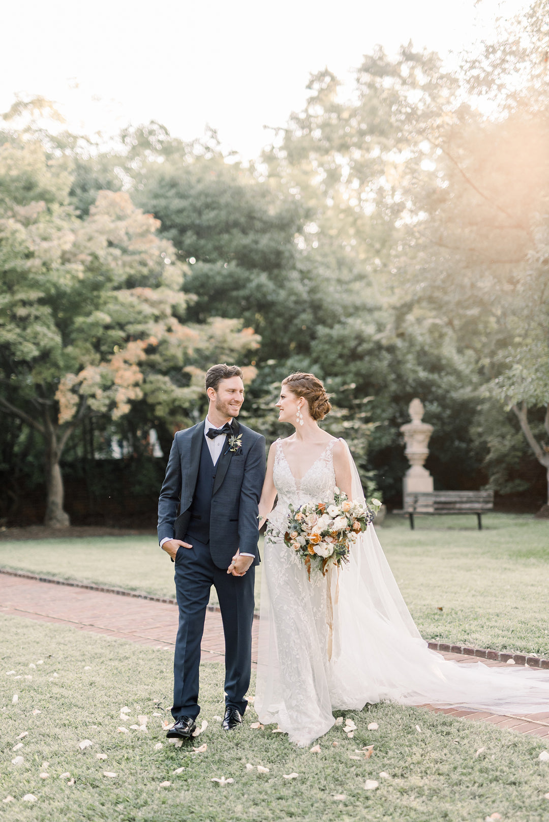 newlywed couple taking photographs in park. the bride is wearing a cape.